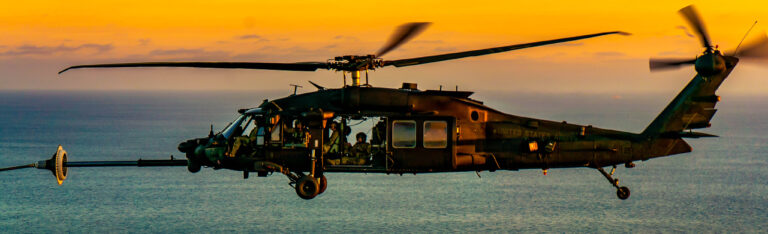 Helicopter flying over ocean at sunset.